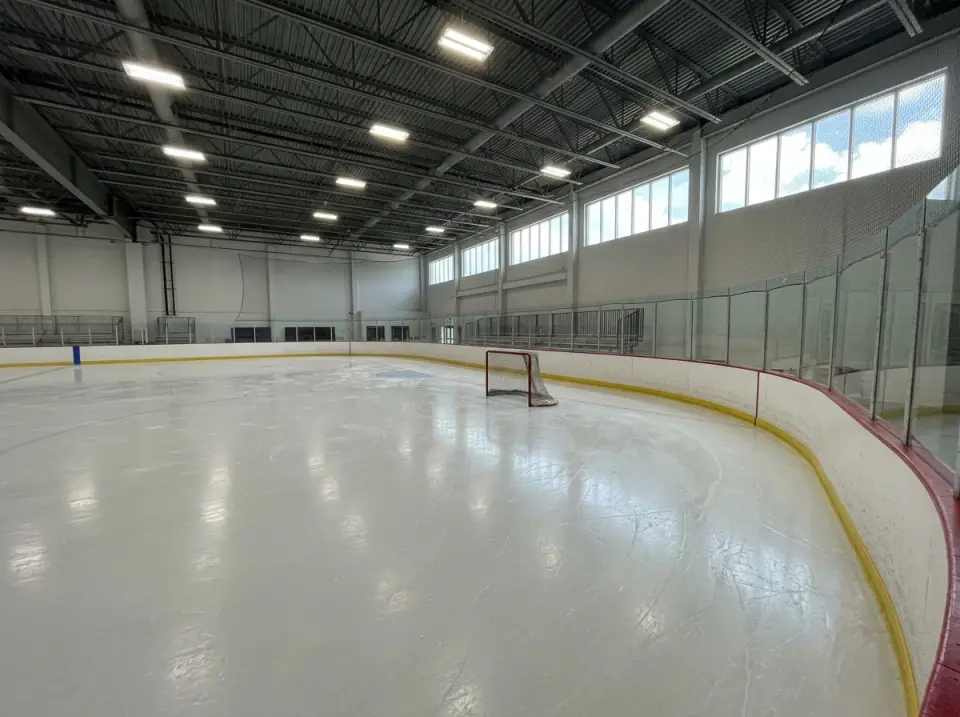 Illustration of an empty indoor ice rink with fresh ice, white boards, a hockey net and glass