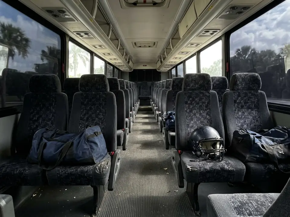 Illustration of the empty aisle of a motorcoach with sports duffel bags and a football helmet on the seats