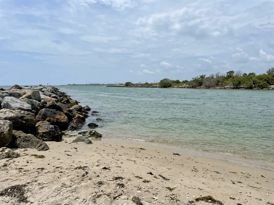 Illustration of the Port Everglades inlet in Fort Lauderdale seen from the beach beside the rock jetty, calm green water in the channel