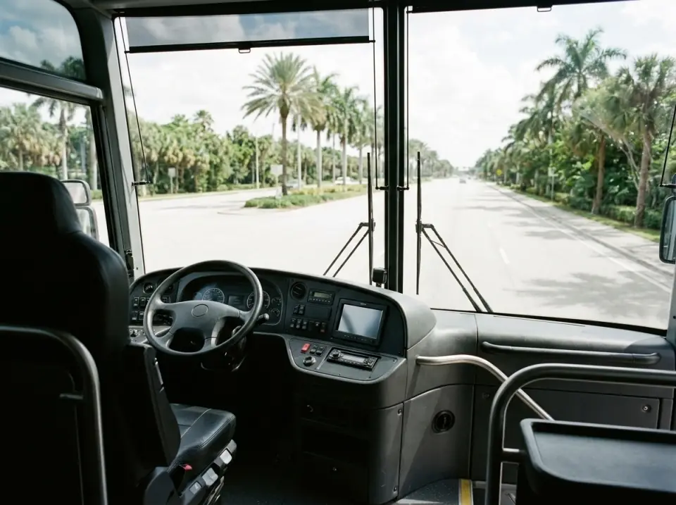 Illustration of the cockpit of a modern motorcoach seen from the front passenger seat, steering wheel and dashboard, with a palm-lined road through the windshield