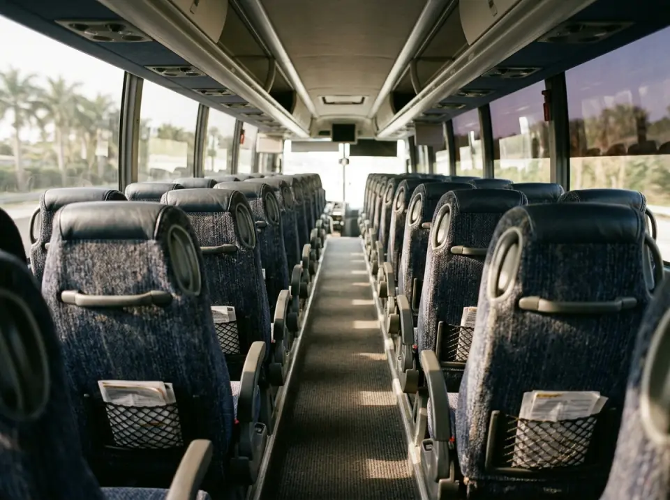 Illustration of rows of plush reclining seats inside an empty full size motorcoach, seen from the aisle, morning light through tinted windows