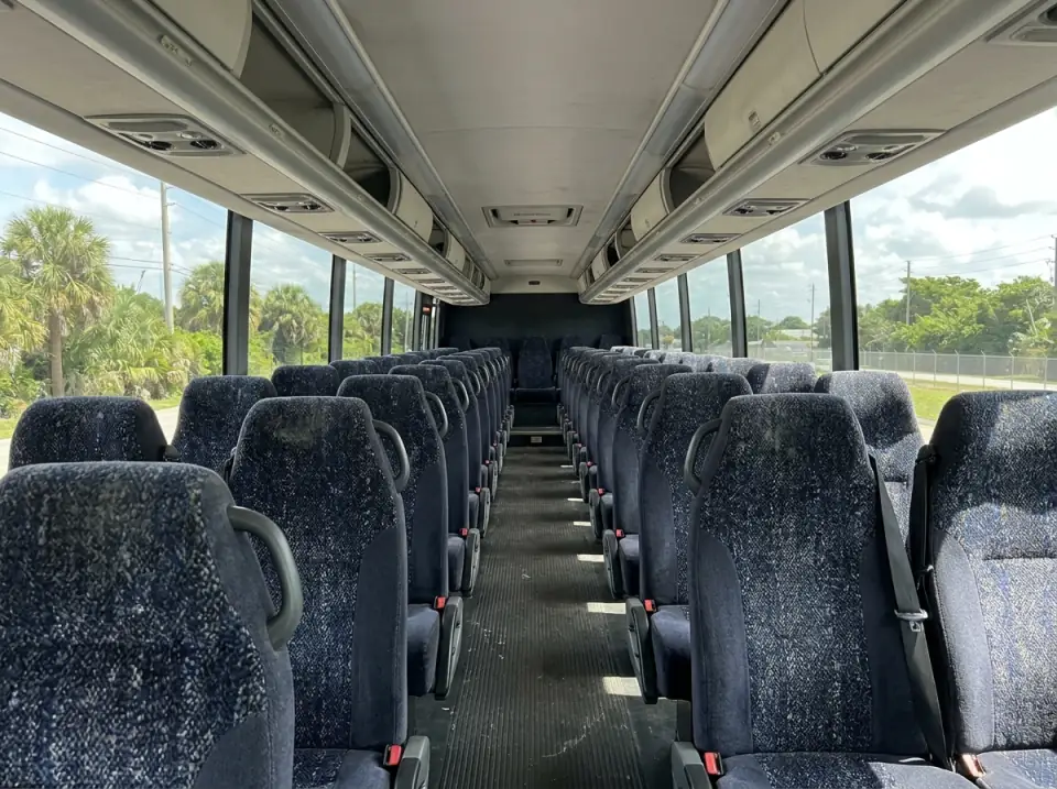 Illustration of the empty interior of a modern motorcoach seen from the aisle, rows of high-back seats under overhead racks and daylight through tinted windows