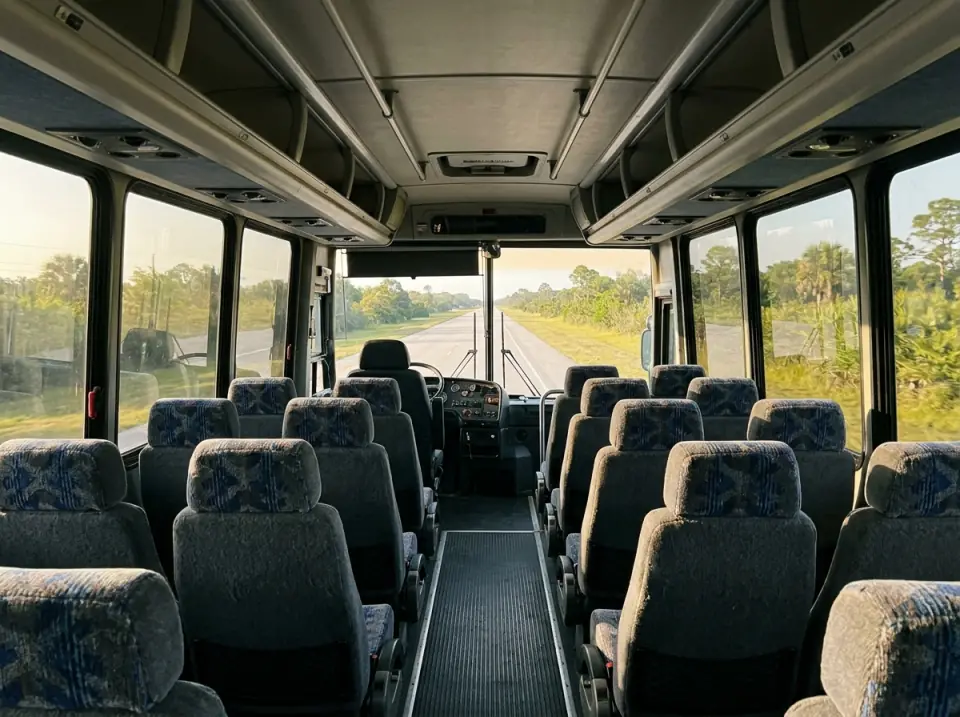 Illustration of the empty interior of a full size motorcoach seen from the rear seats toward the windshield, a straight Florida road ahead in morning light