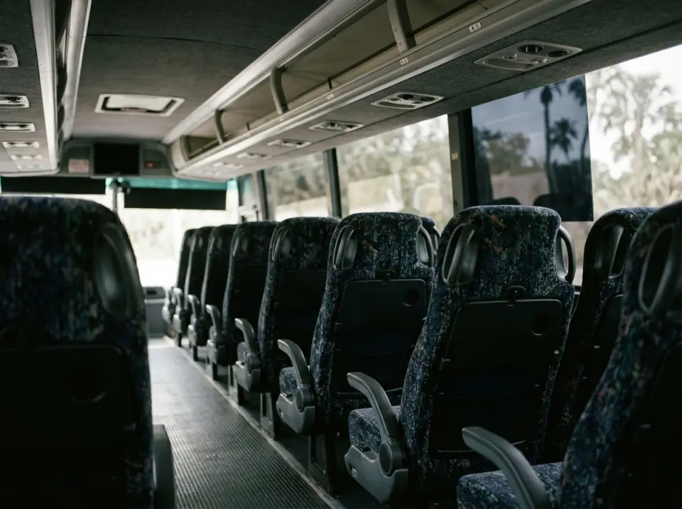Illustration of the overhead luggage racks and reclining seats of a motorcoach seen from the aisle, soft light through tinted windows