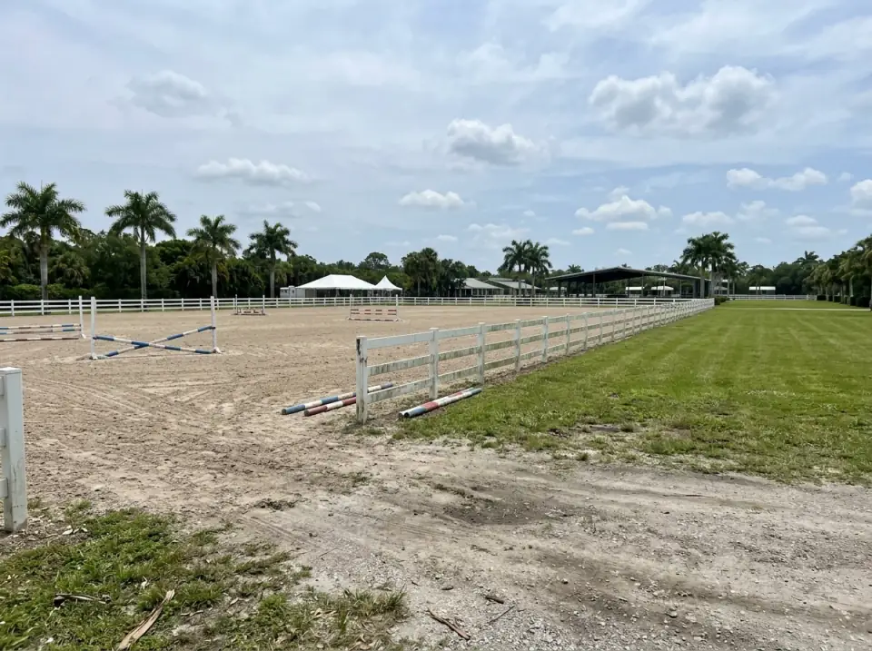 Illustration of equestrian show grounds in Wellington west of West Palm Beach, white rail fences around a sand arena with jump poles and palms beyond