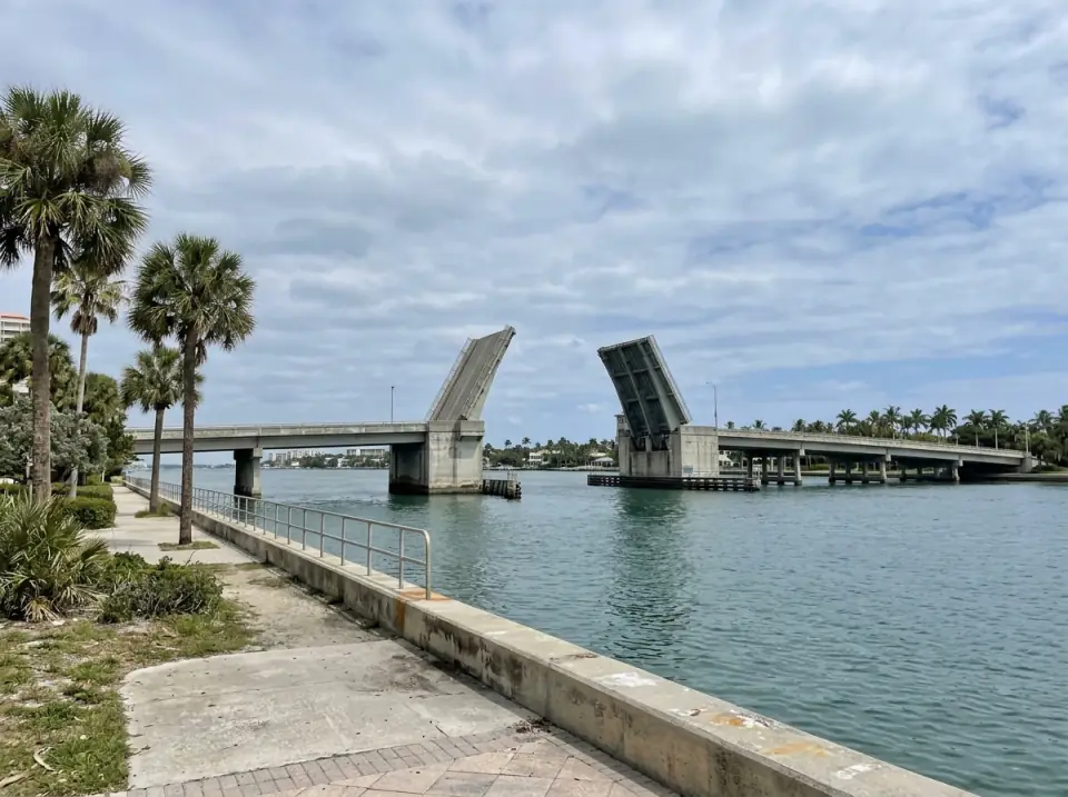 Illustration of a drawbridge with both leaves raised over the Lake Worth Lagoon between West Palm Beach and Palm Beach, seen from the waterfront path