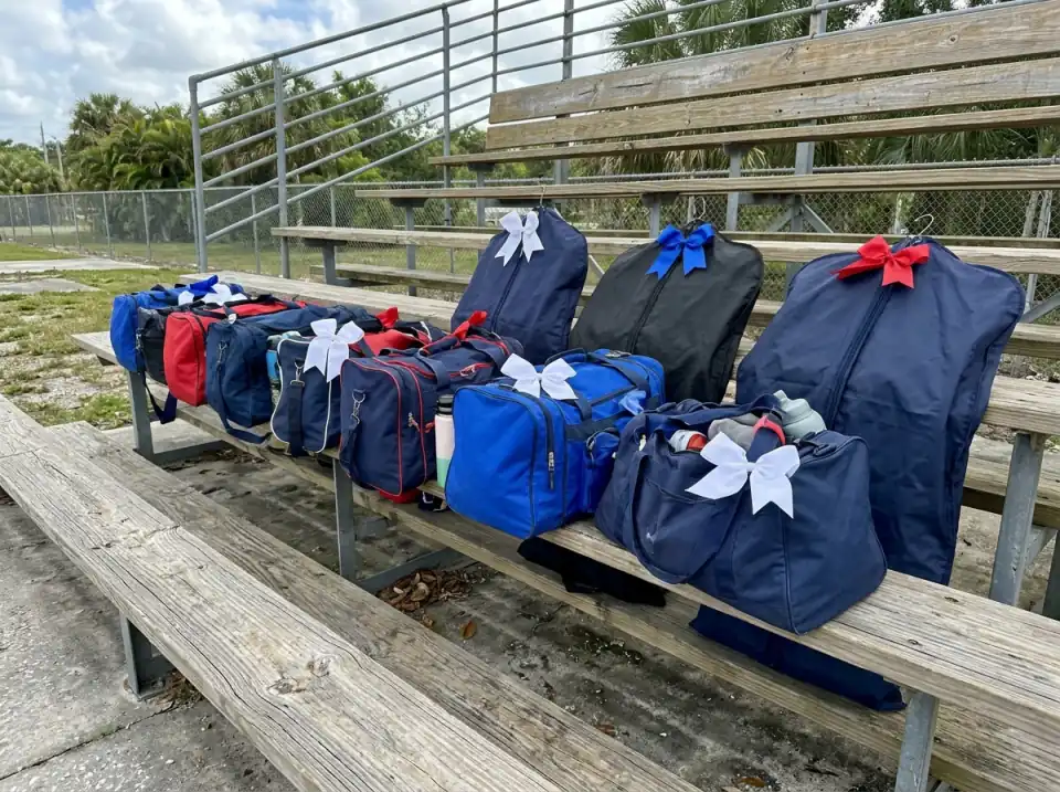 Illustration of cheer duffel bags and dark garment bags with ribbon bows lined up on a wooden bleacher bench