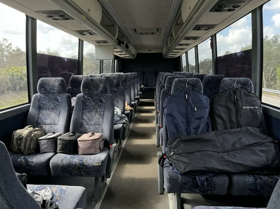 Illustration of the empty aisle of a motorcoach with dark garment bags laid across seats and small makeup cases on others