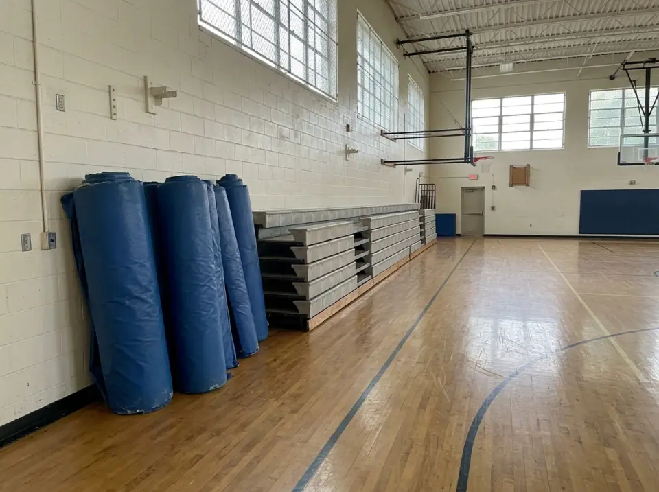 Illustration of blue gym mats rolled up along the wall of a school gym with folded bleachers