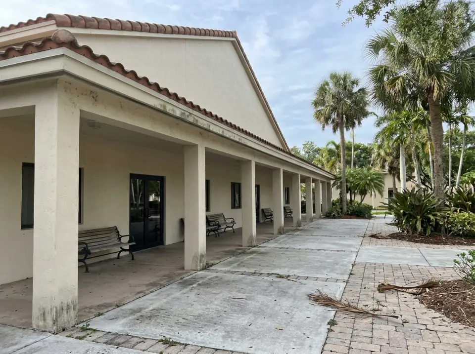 Illustration of a covered walkway with benches along the side of a South Florida church building, palms and a wide paved area beside it