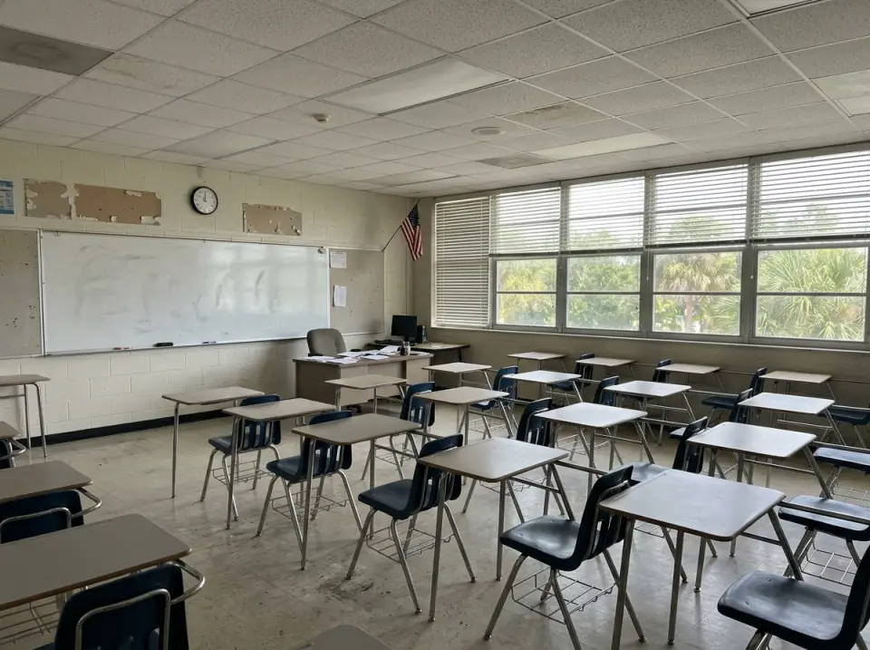 Illustration of an empty high school classroom with rows of desks, a wiped whiteboard and half-open blinds