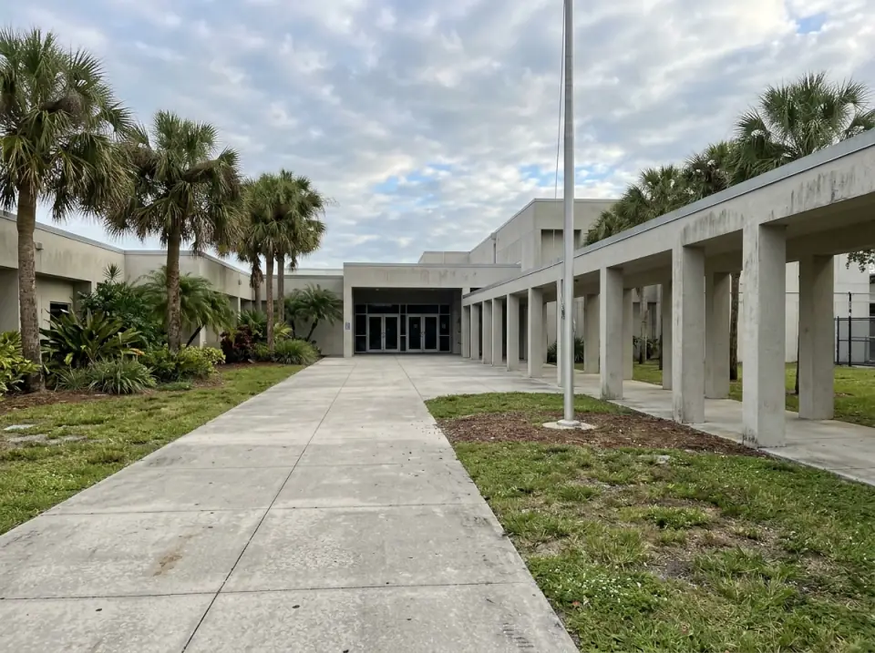 Illustration of the empty front walkway of a South Florida high school with palms, a covered breezeway and a bare flagpole in morning light