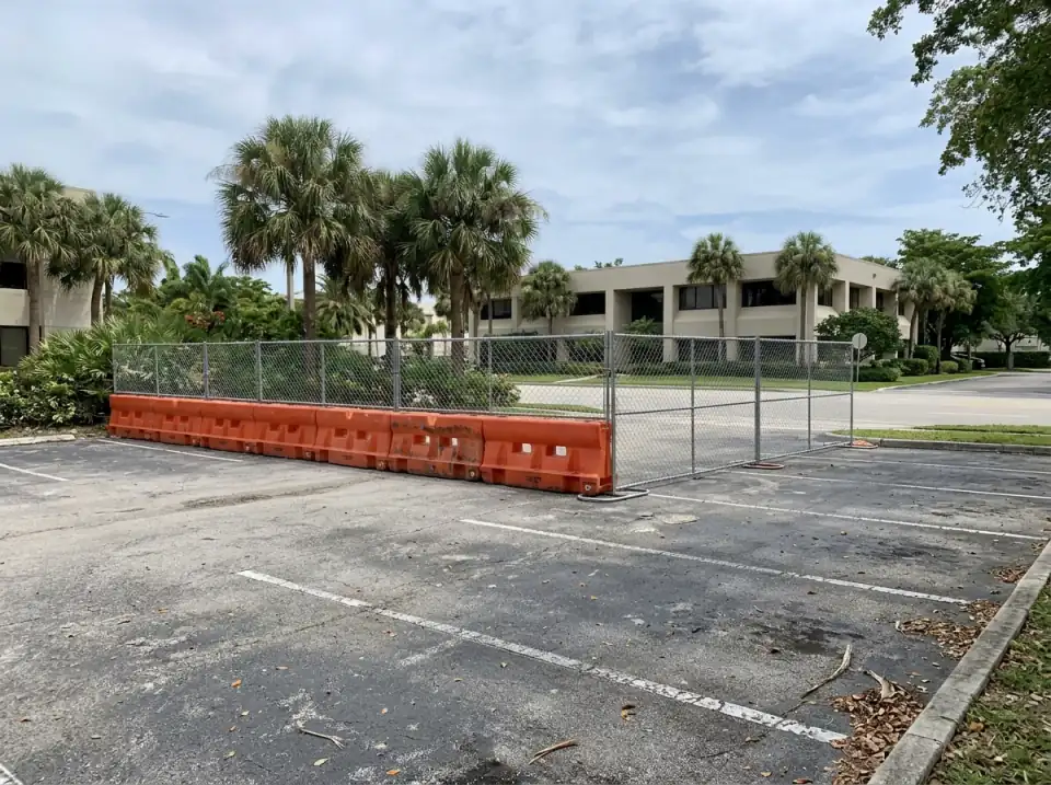 Illustration of a corner of an empty office parking lot closed off with orange barriers and construction fencing, palms and a low office building behind