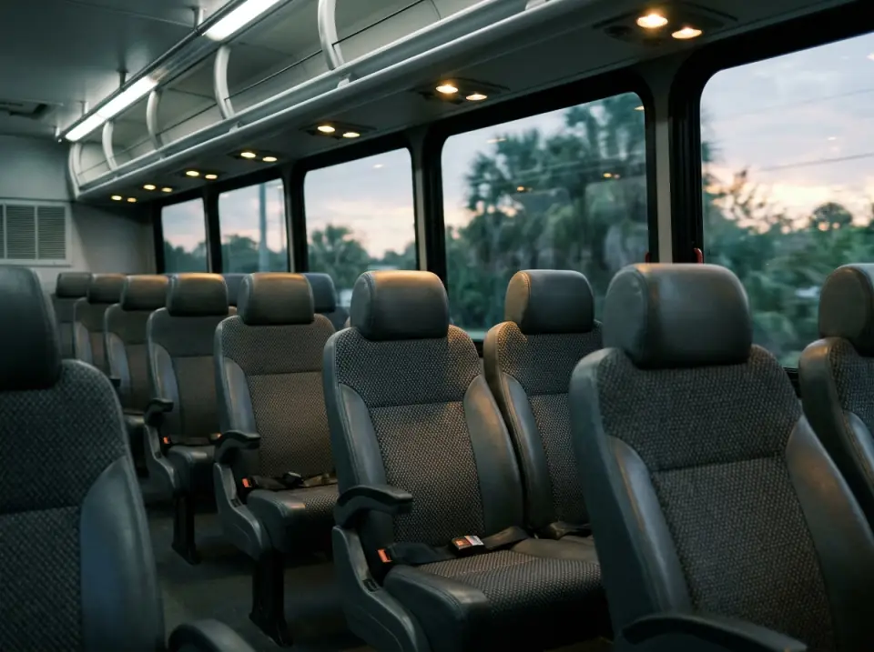 Illustration of a row of empty dark grey reclining seats inside a commuter coach in the early morning, reading lights on