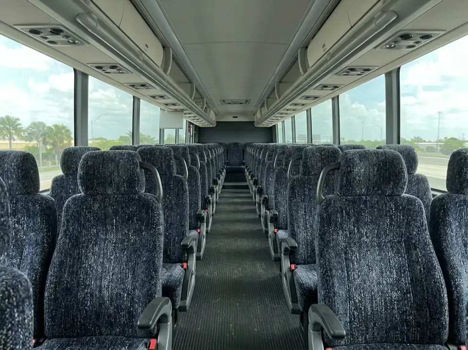 Illustration of the empty interior of a full size motorcoach seen from the aisle, rows of high-back seats under overhead racks
