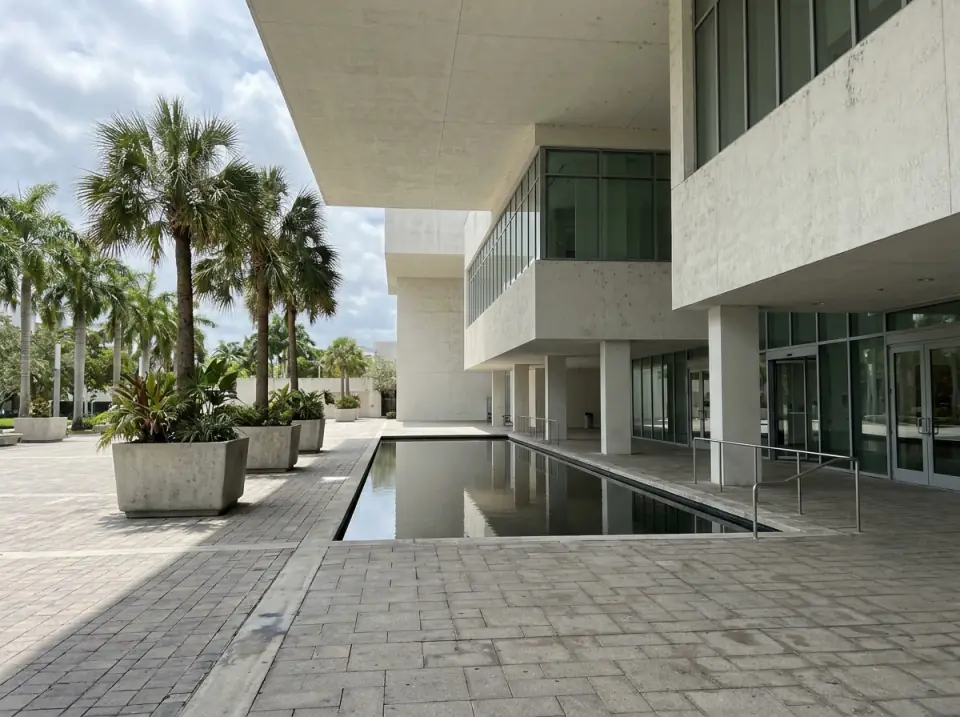 Illustration of the shaded entrance plaza of a modern museum building in Miami, white concrete and glass, palms in planters and a shallow reflecting pool
