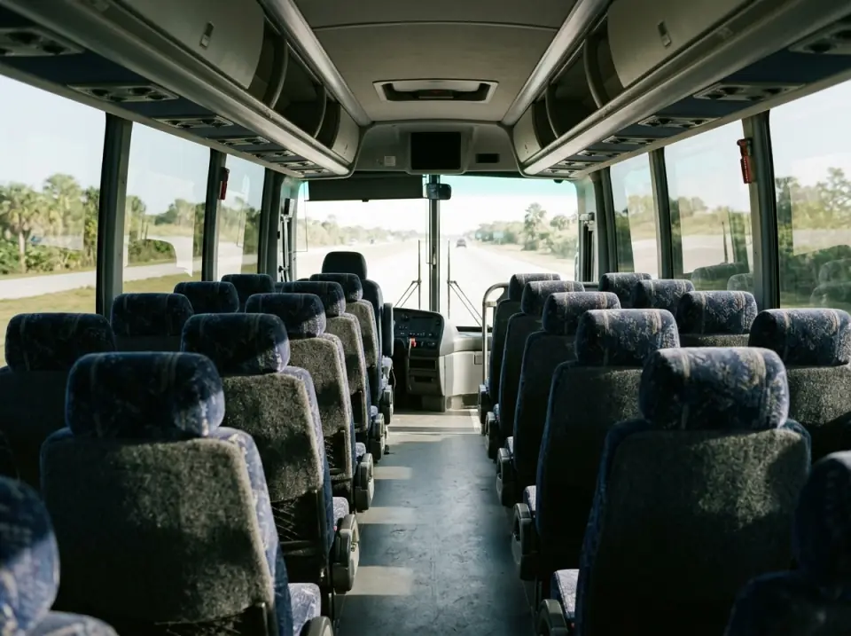 Illustration of the interior of a motorcoach seen from the rear seats toward the front, tinted windows and morning light
