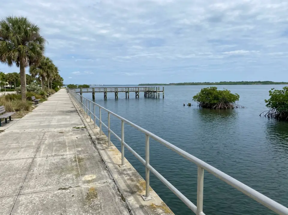 Illustration of the wide, calm Indian River Lagoon seen from a downtown Fort Pierce seawall walk, with mangrove islets and a wooden fishing pier