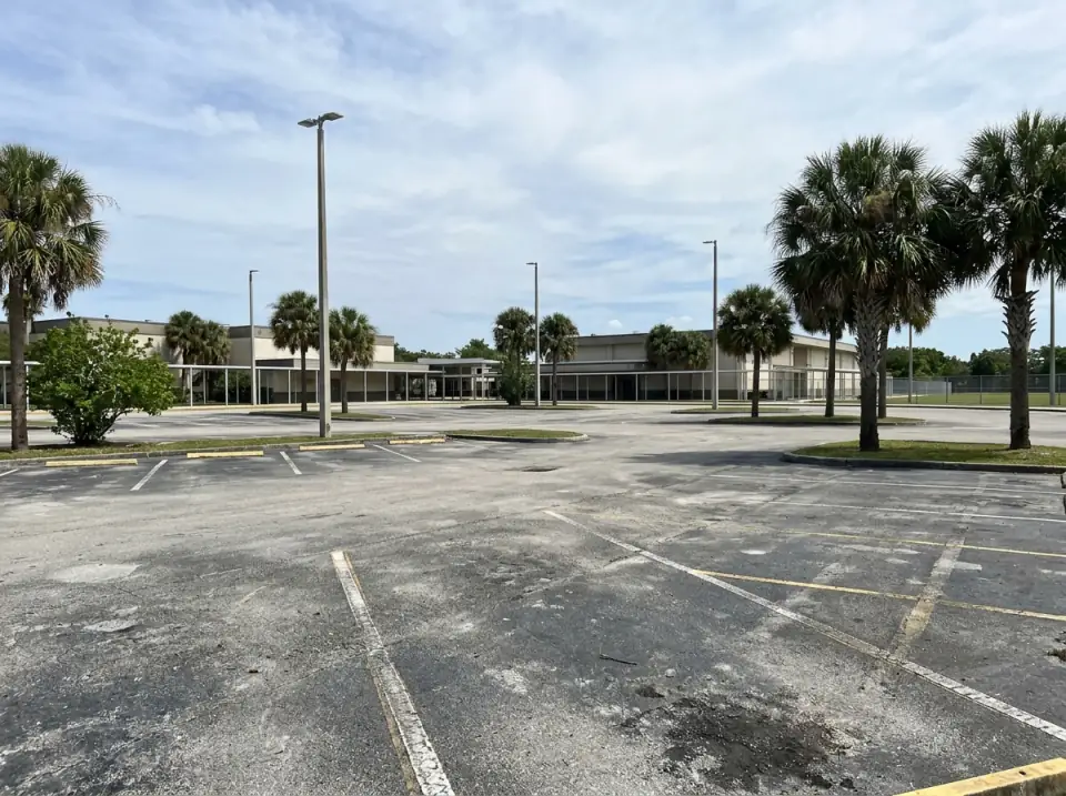 Illustration of a quiet high school parking lot with tall light poles, palms and empty striped spaces under a bright afternoon sky