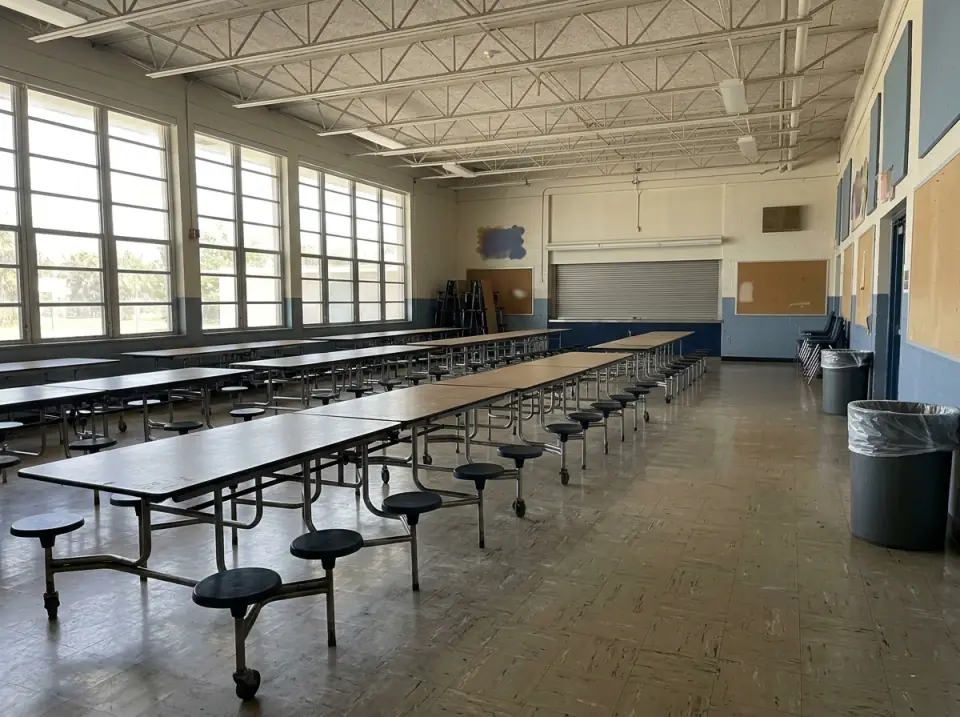 Illustration of an empty school cafeteria with long tables and stools, daylight through tall windows