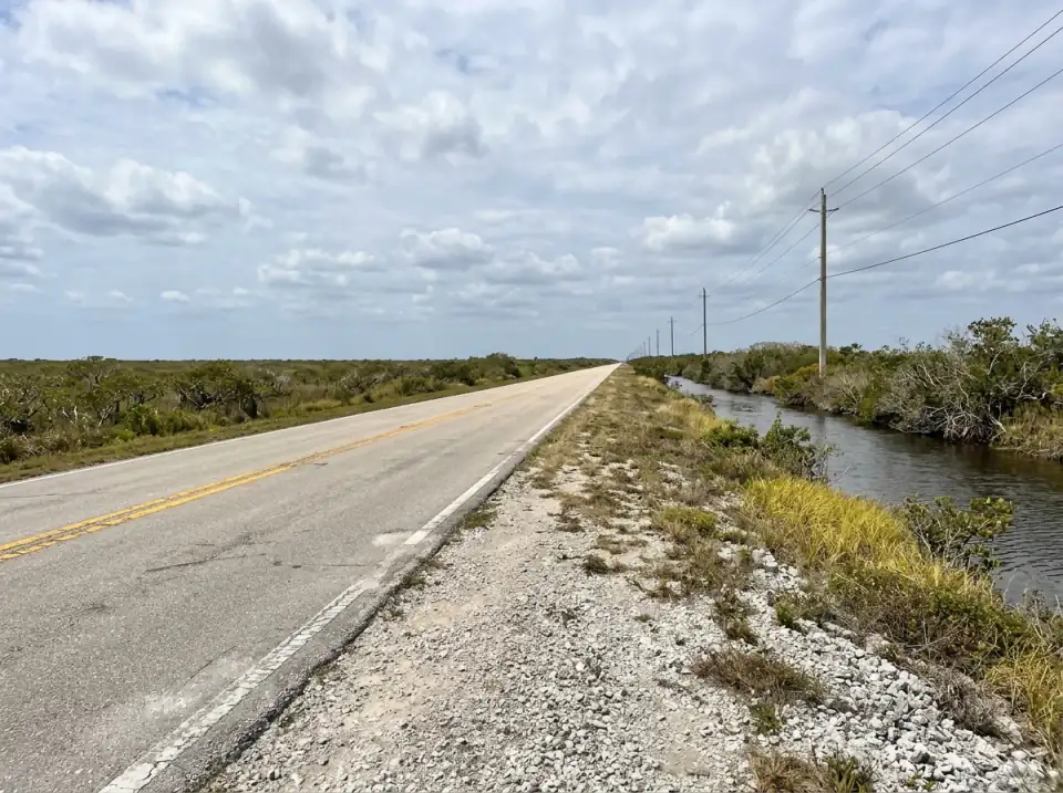 Illustration of an empty two-lane road heading south from Florida City through flat mangrove and sawgrass, with a canal alongside