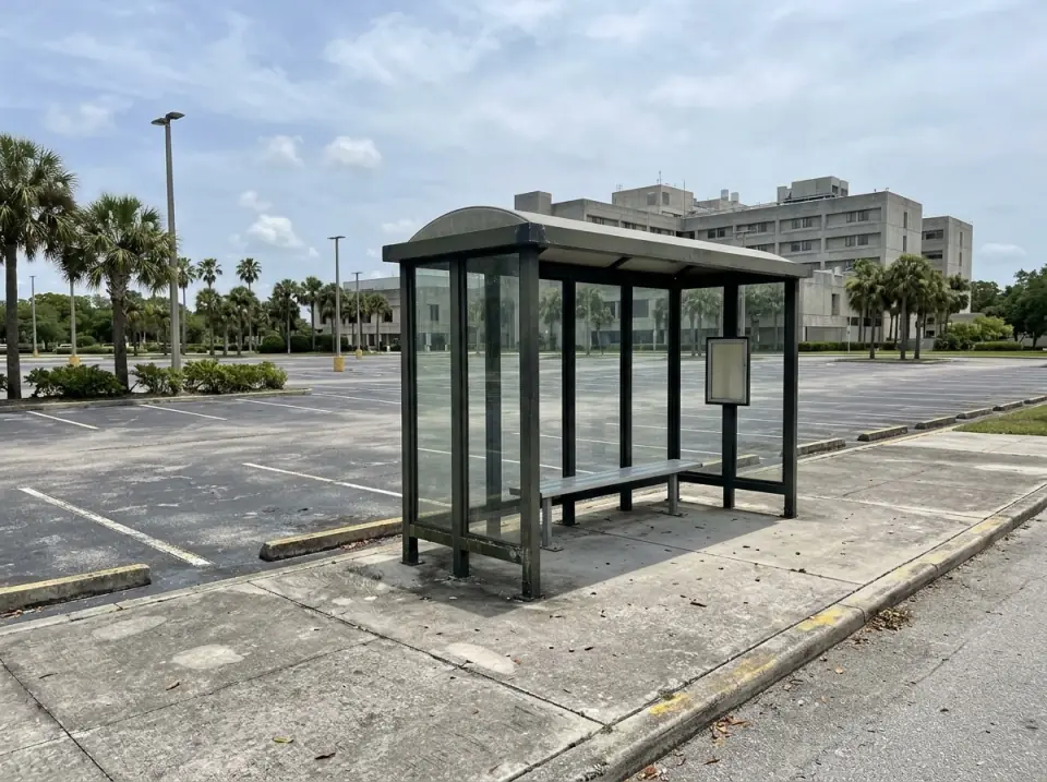 Illustration of an empty covered shuttle shelter with a bench at the edge of a large staff parking lot, palms and a hospital campus building in the distance
