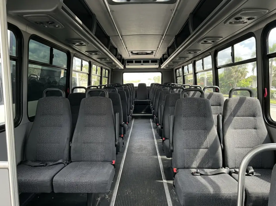 Illustration of the empty interior of a modern minibus seen from the aisle, high-back seats on both sides and daylight through tinted windows