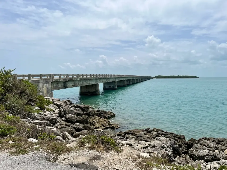 Illustration of a long, low concrete bridge running across turquoise water in the Middle Keys, seen from a rocky shoreline pull-off in Marathon