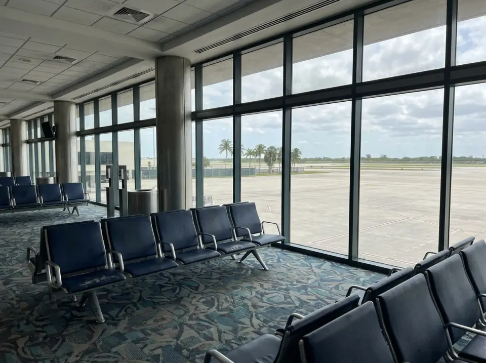 Illustration of a quiet airport gate area with rows of empty blue seats facing tall windows and palms beyond the apron