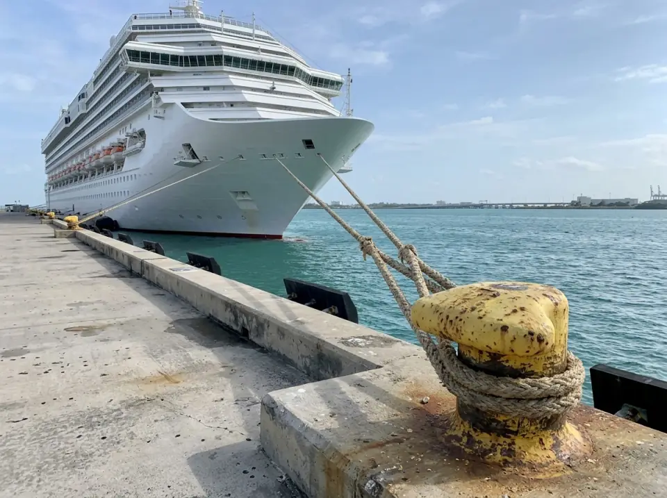 Illustration of a white cruise ship docked at a PortMiami pier, a yellow bollard with a mooring line in the foreground and turquoise bay water alongside