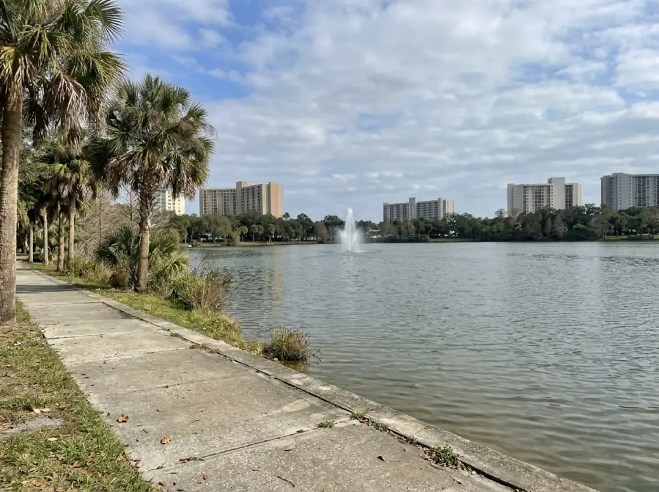 Illustration of a calm Orlando lake with a fountain in the middle, palms along a lakeside path and hotel towers across the water