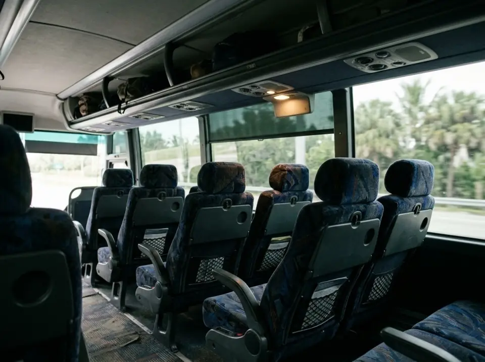 Illustration of the overhead luggage racks and reclining seats inside a motorcoach, a reading light on and soft daylight through tinted windows