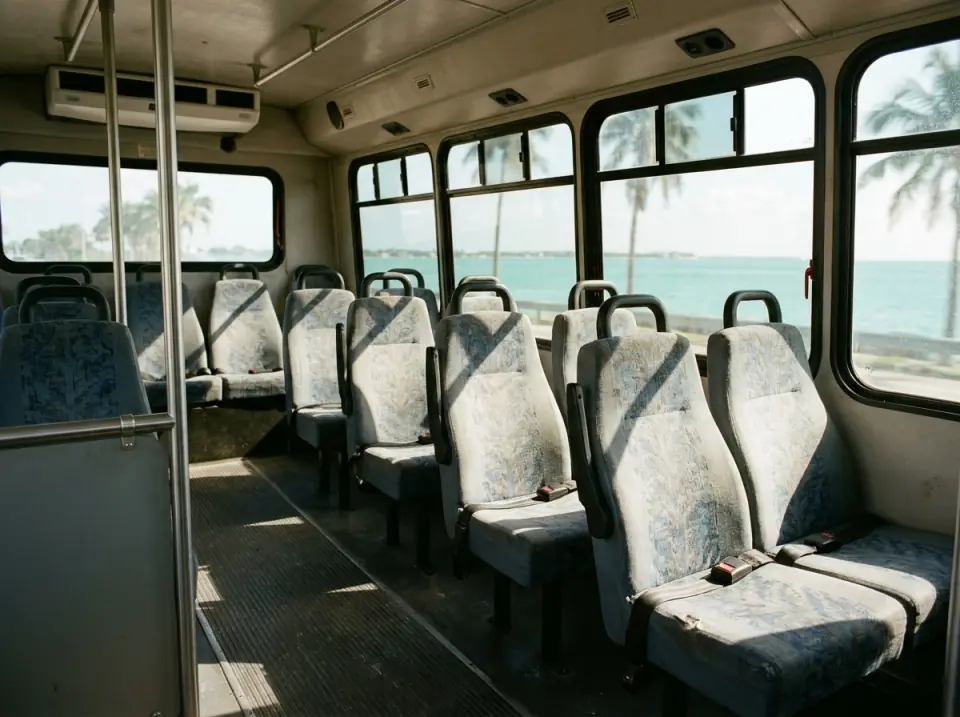 Illustration of the empty interior of a minibus with sunlight on the seats and turquoise water visible through the tinted windows
