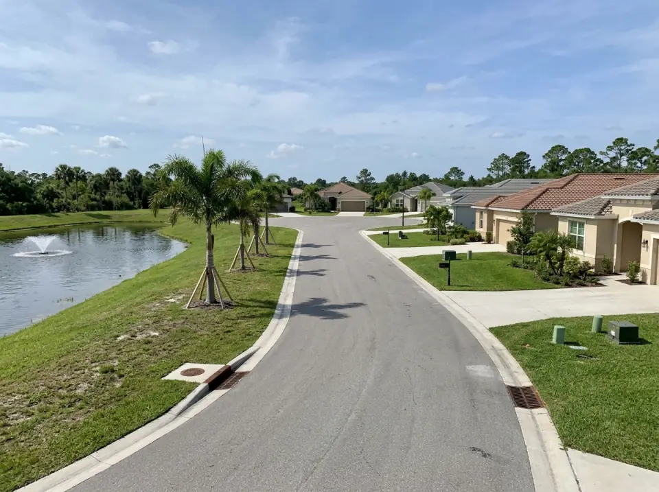 Illustration of a curving street in a newer Port St. Lucie neighborhood, a stormwater lake with a fountain on one side and single-story tile-roof homes on the other