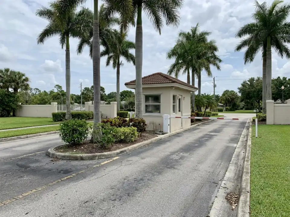 Illustration of the entrance of a gated community in Port St. Lucie, a small gatehouse with a lowered barrier arm between royal palms