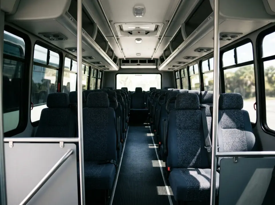Illustration of the empty interior of a modern 20 seat minibus seen from the front, high-back seats on each side of a narrow aisle under overhead racks