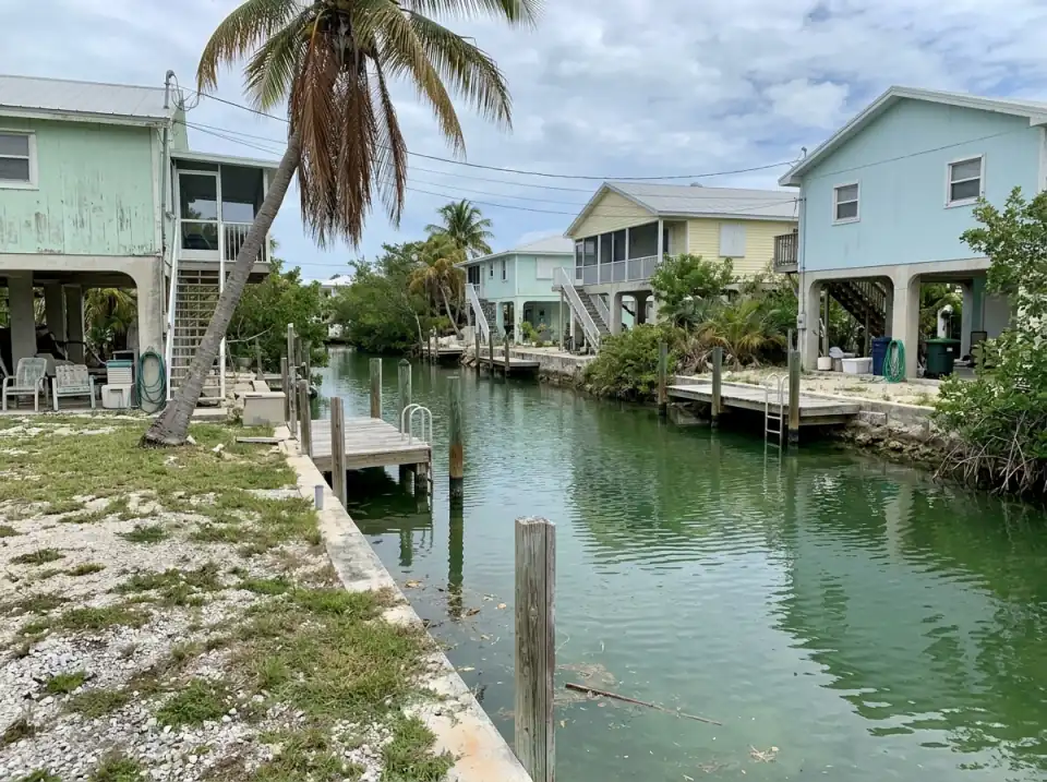 Illustration of a quiet Florida Keys canal lined with raised pastel stilt houses, small wooden docks and coconut palms