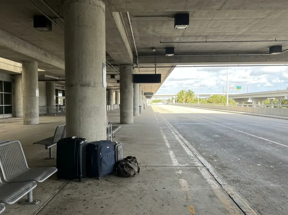 Illustration of suitcases and a duffel bag beside a concrete column and metal benches at a covered airport ground transportation pickup area