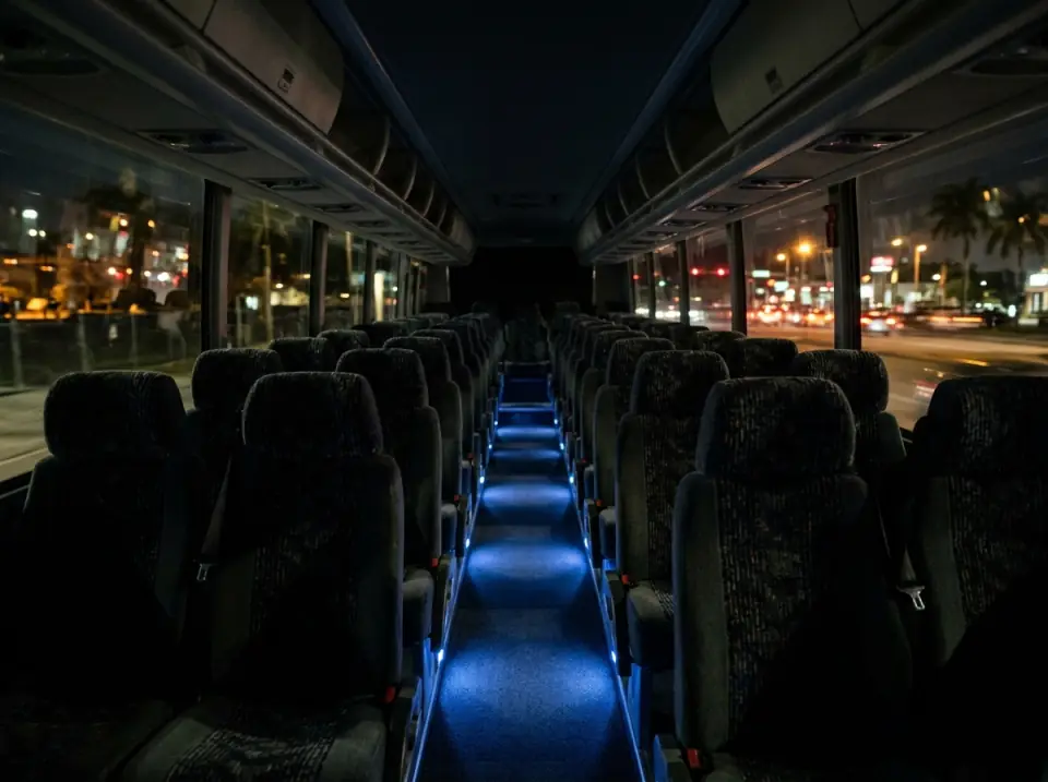 Illustration of the interior of a motorcoach at night with soft blue aisle lights, empty seats and city lights blurred outside the windows