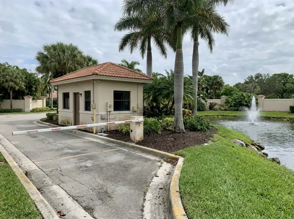 Illustration of a gated community entrance in Pembroke Pines, with a small guardhouse, a lowered gate arm, royal palms and a fountain pond