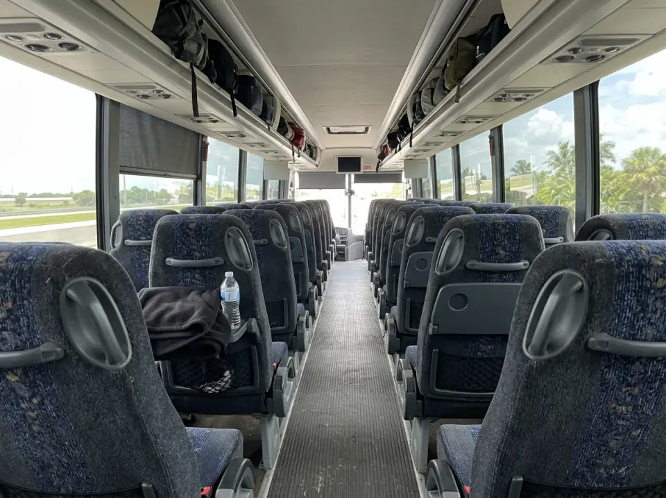Illustration of the empty aisle of a motorcoach with reclining seats, a folded blanket and a water bottle on one seat and carry-on bags in the overhead racks