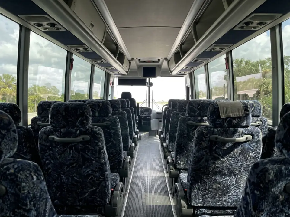 Illustration of the empty interior of a motorcoach seen from the back of the aisle, rows of seats and daylight through tinted side windows
