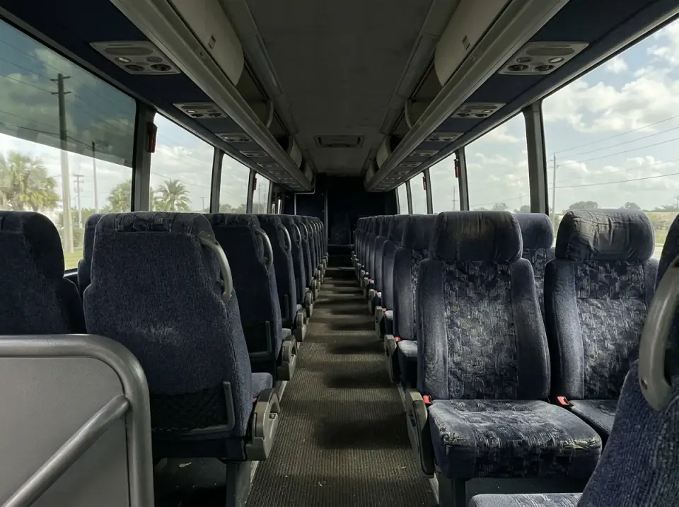 Illustration of the empty interior of a motorcoach seen from the front of the aisle, high-back cloth seats on both sides under overhead racks