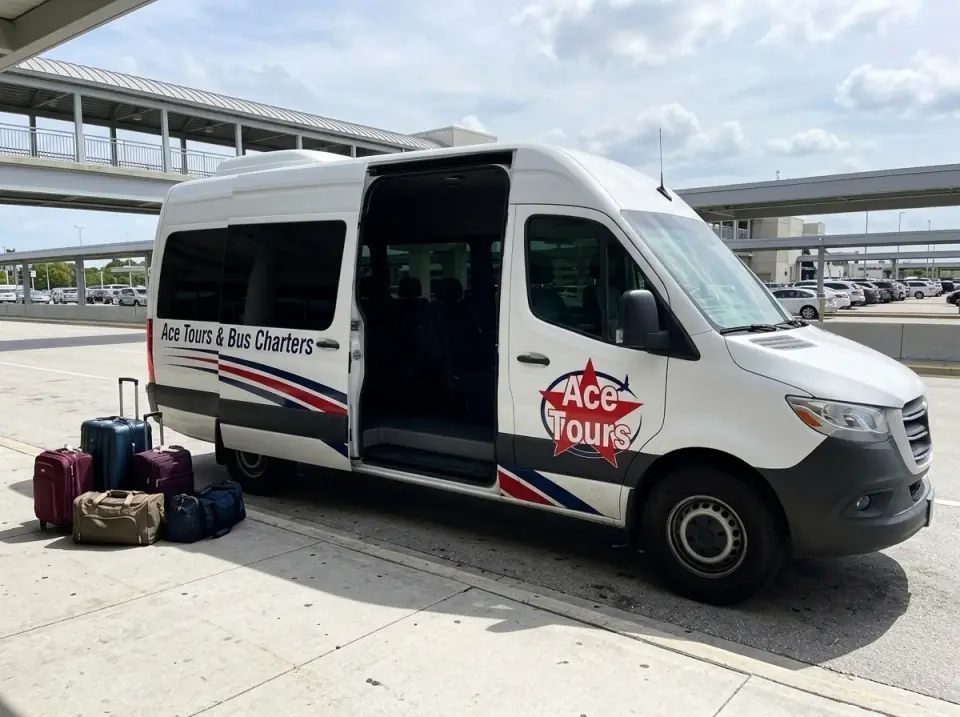 Illustration of a white Ace Tours & Bus Charters Sprinter-style van at a Miami airport arrivals curb, sliding door open, suitcases on the curb