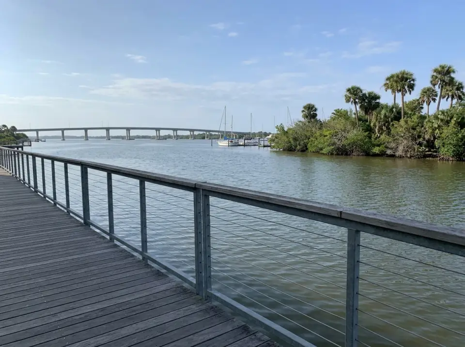Illustration of the St. Lucie River in Stuart seen from the downtown riverwalk, sailboats moored and a long bridge in the distance