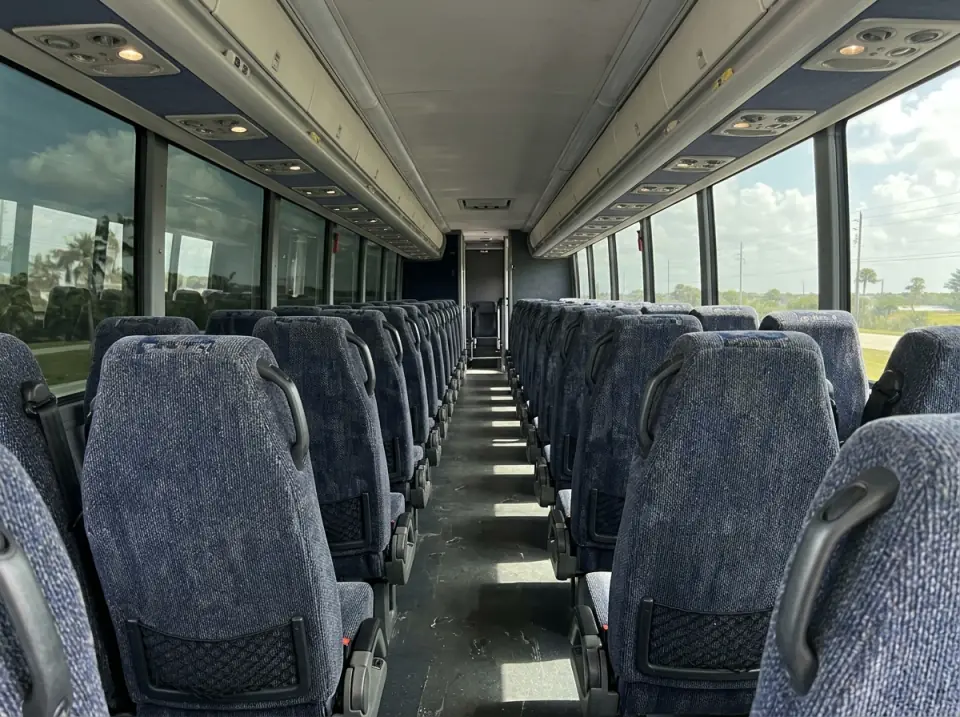 Illustration of the empty interior of a modern motorcoach seen from the front of the aisle, rows of high-back fabric seats and daylight through tinted windows