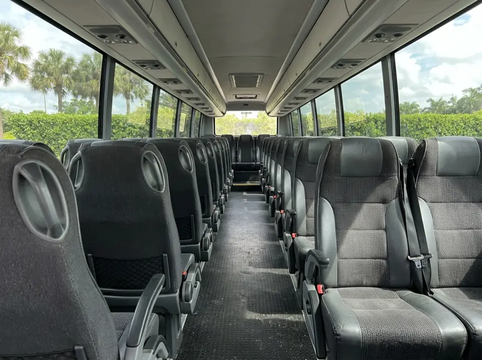 Illustration of the empty interior of a coach seen from the aisle, dark grey high-back seats on both sides under overhead racks
