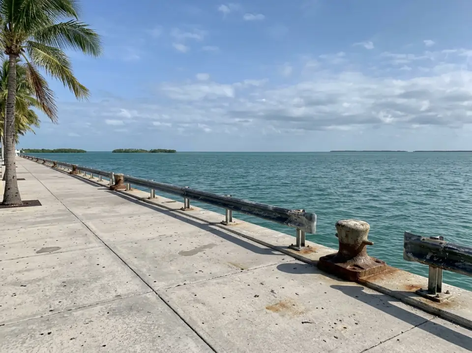 Illustration of a seawall promenade on the Key West waterfront looking west over open water to small mangrove islands in the afternoon